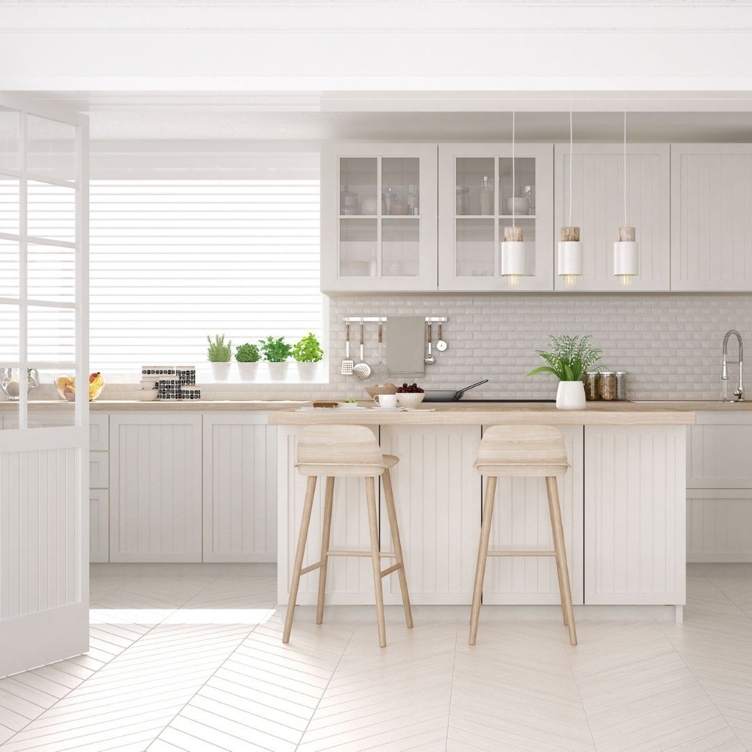 A photo of a modern kitchen. The floor is tiled and it is white, the walls are also white. The top and floor kitchen units are white and there is also a handy island in the middle with two stools.